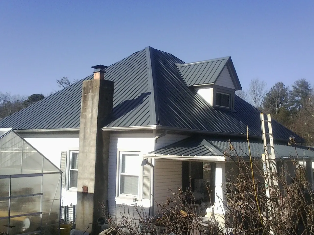 Dark blue standing seam metal roof on a white farmhouse with dormer — Slate & Tile Roof Repair by Roofing Brothers in Zion Grove