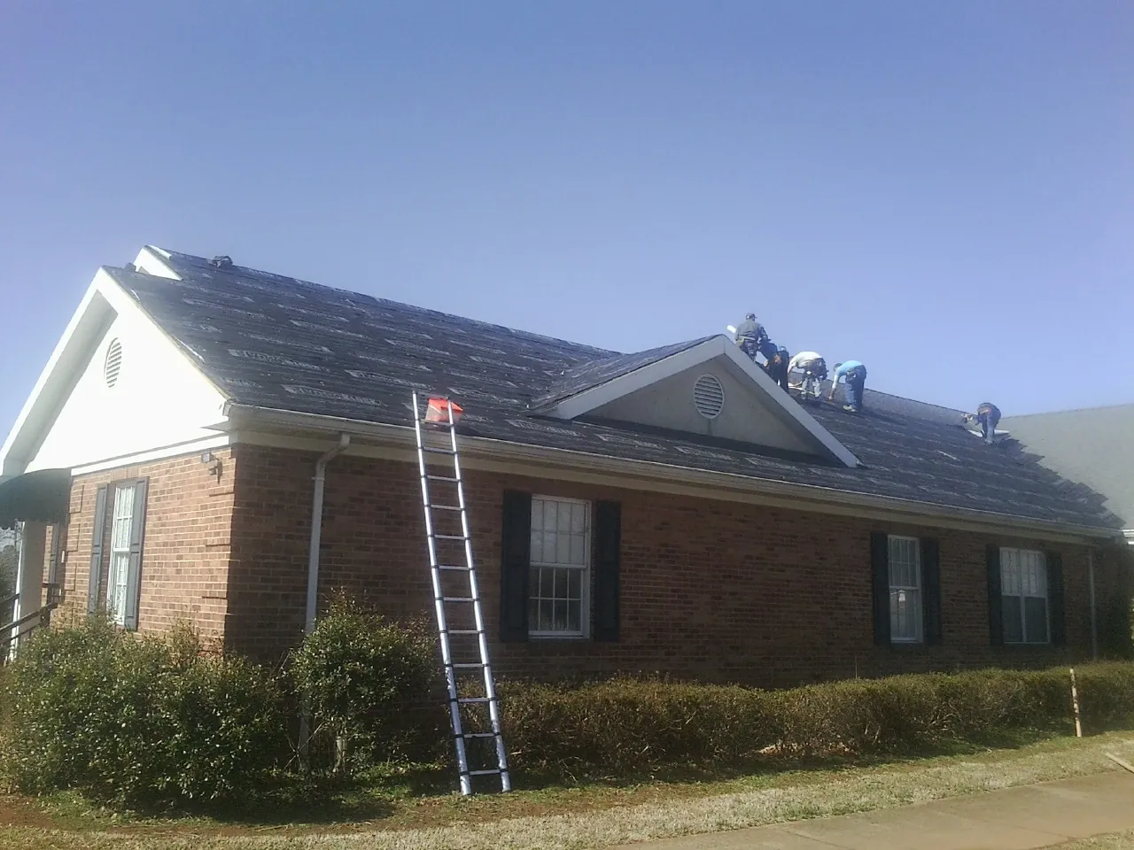 Crew tearing shingles off a brick ranch roof with a ladder set — Metal Roof Repair work by our crew in Zion Grove