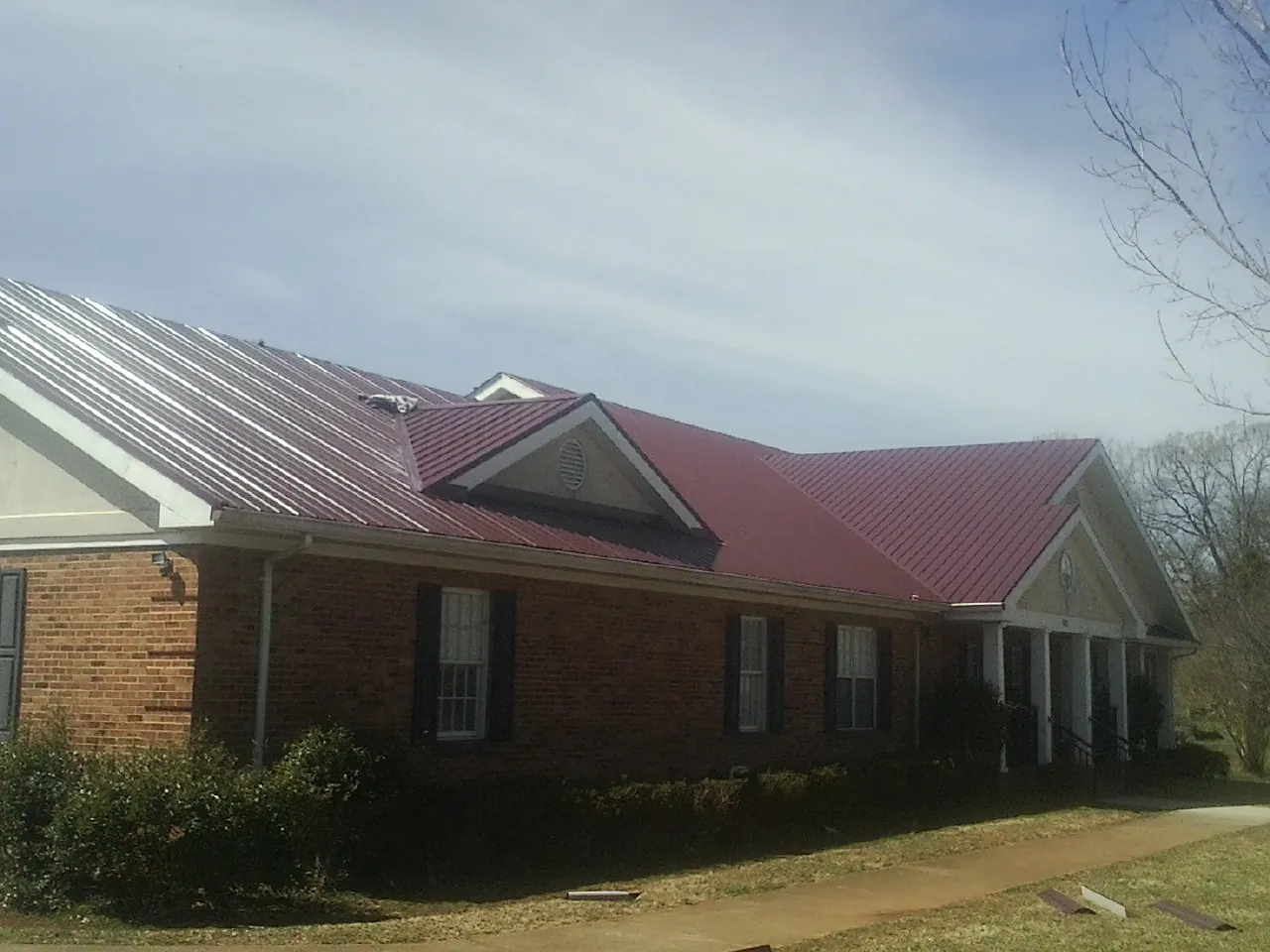 Red metal roof with gabled entries on a long brick building, from a Hail Damage Roof Repair job in Zion Grove