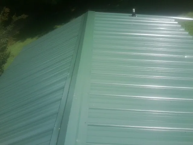 New green metal panels meeting at the ridge of a roof — Flat Roof Repair work by our crew in Zion Grove
