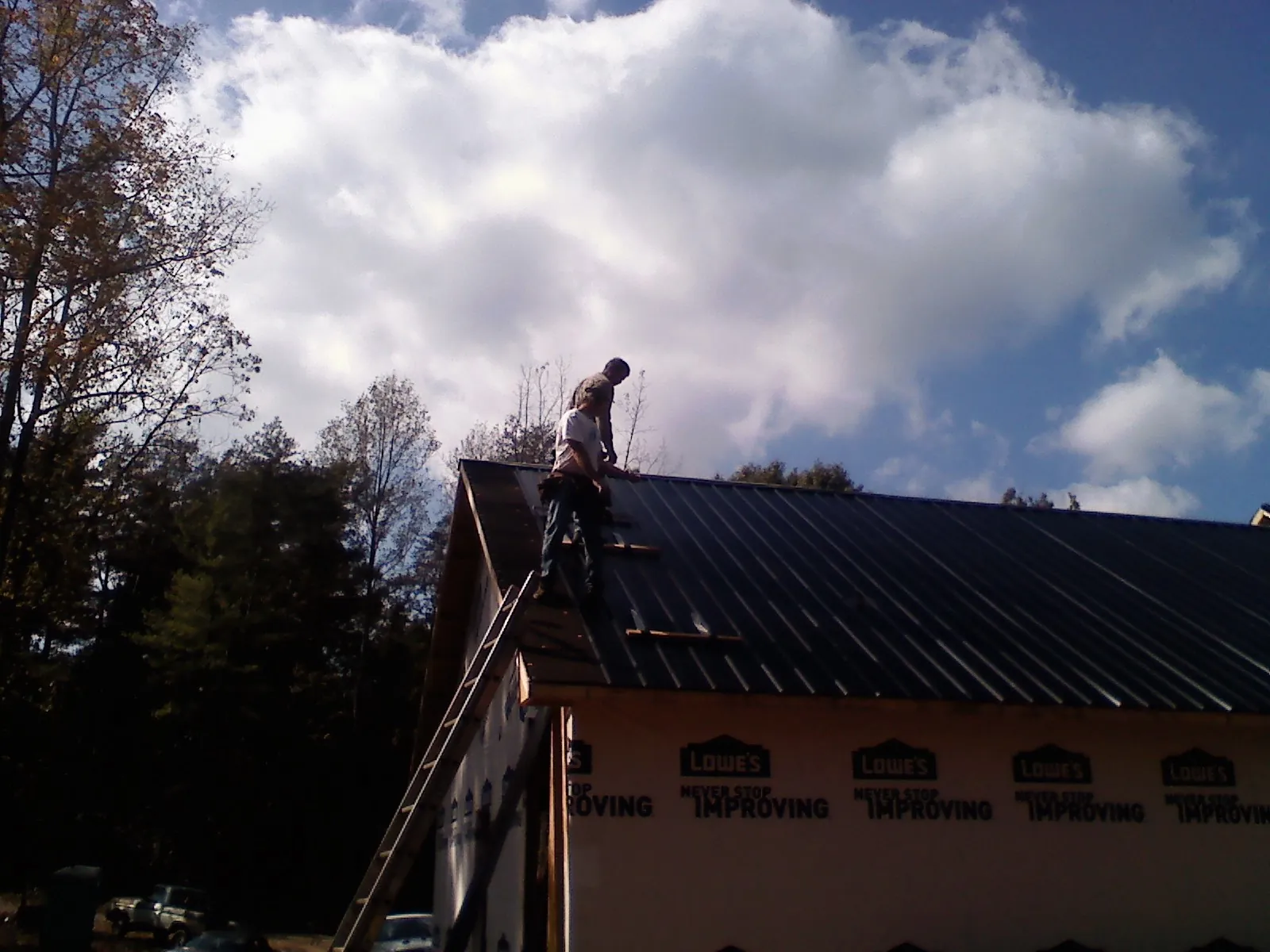 Roofer fastening dark metal panels high against a cloudy sky, from a Roof Inspection job in Zion Grove