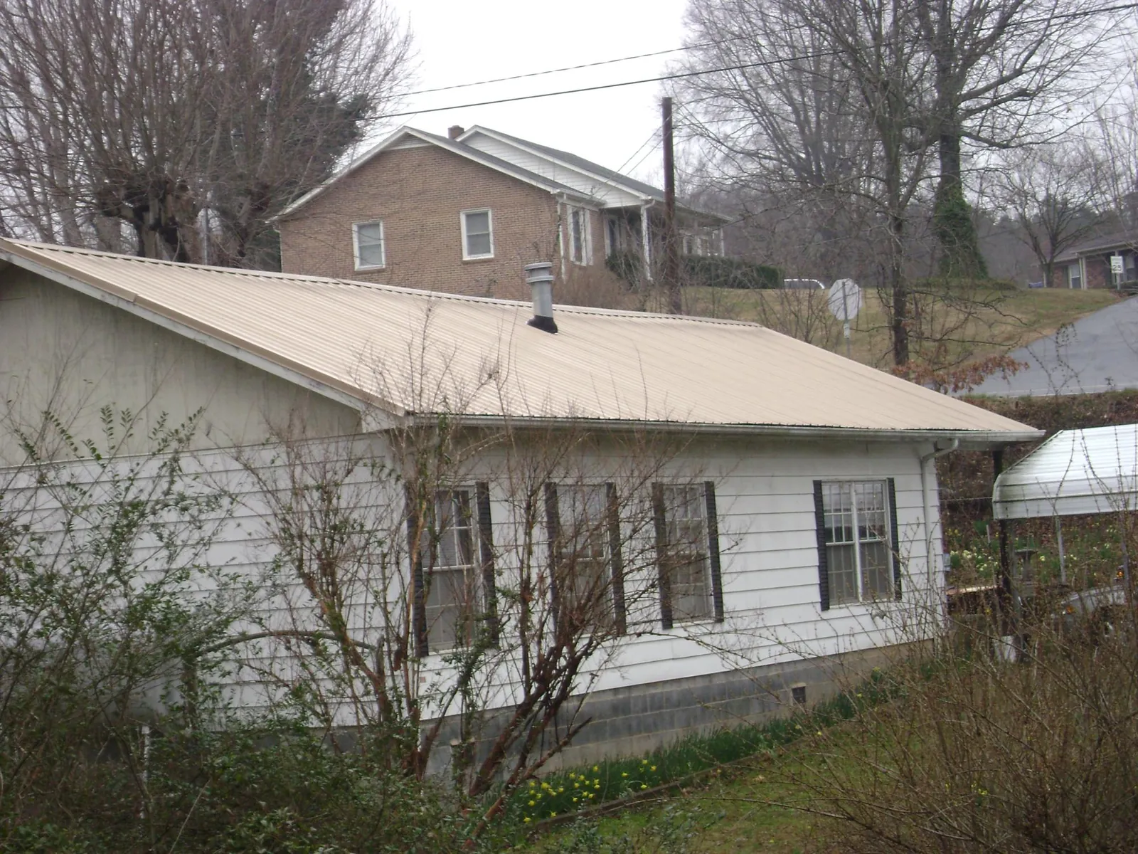 Tan metal roof on a white sided house set into a hillside — Commercial Roofing by Roofing Brothers in Zion Grove